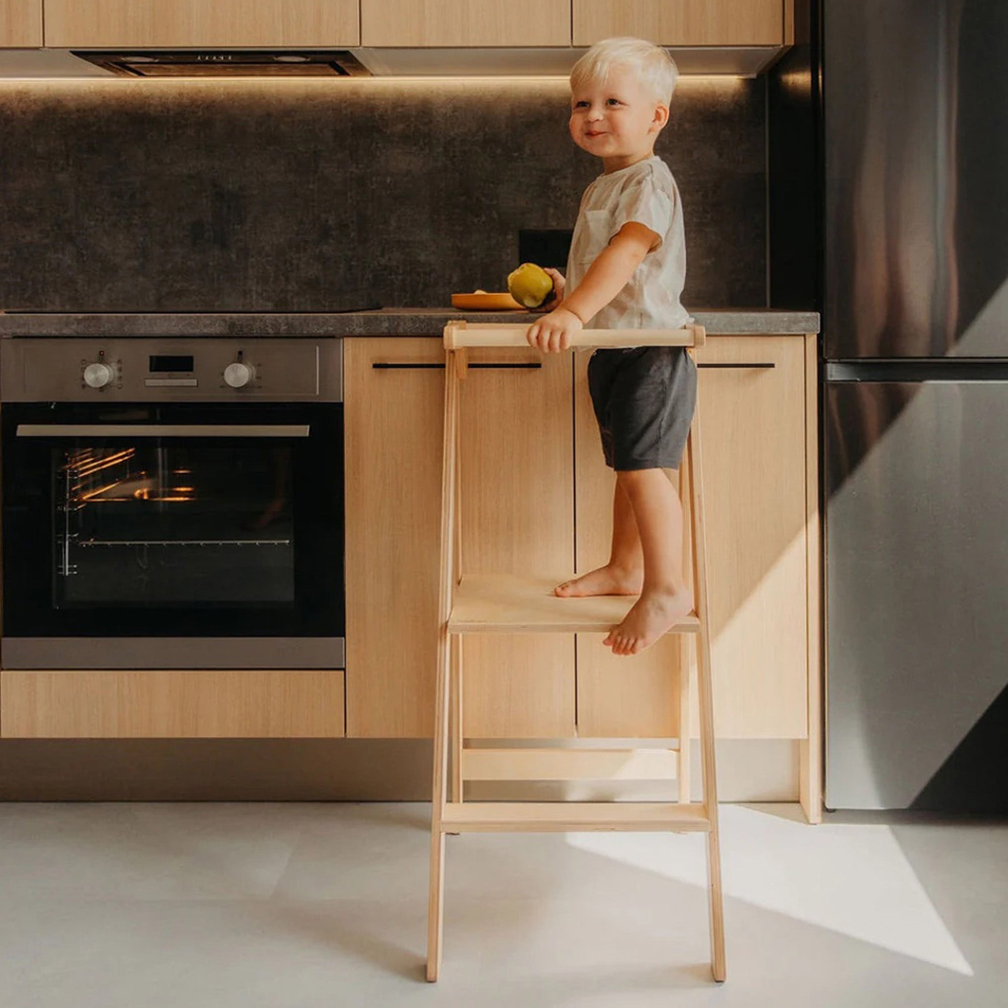 Toddler climbing into Roomix foldable learning tower, illustrating child independence and safe interaction